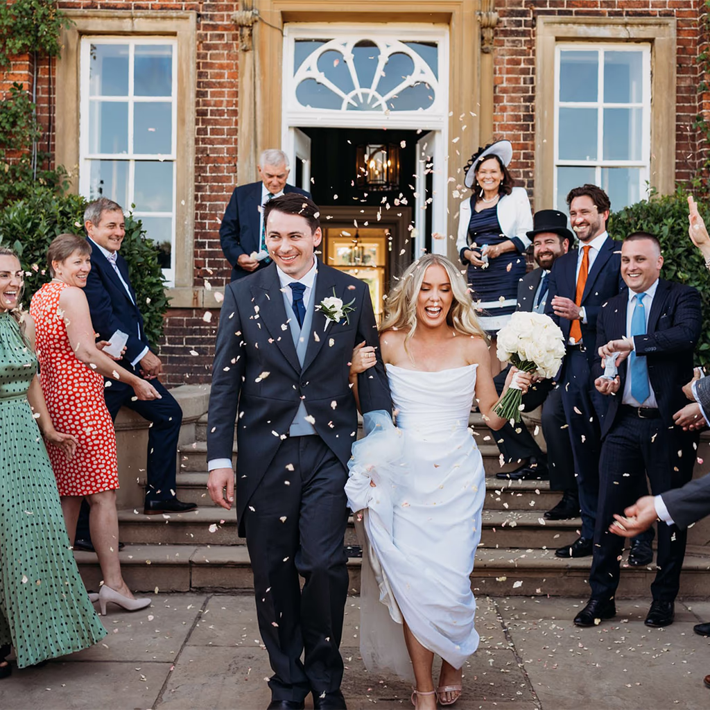 A bride and groom walk outside Norwood Park, Nottinghamshire, smiling as guests throw confetti.
