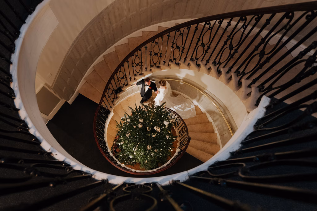 A bride and groom walking down a spiral staircase with a christmas tree in the centre.