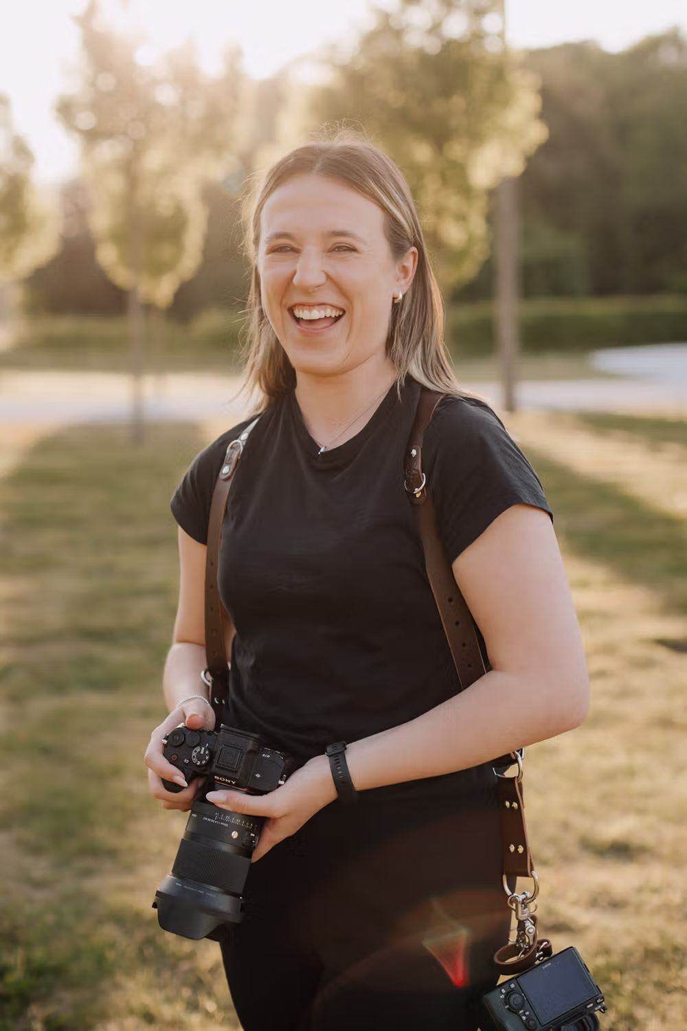 Mel at Hazel Gap Barn, holding a camera in her hand with the golden hour sun behind her