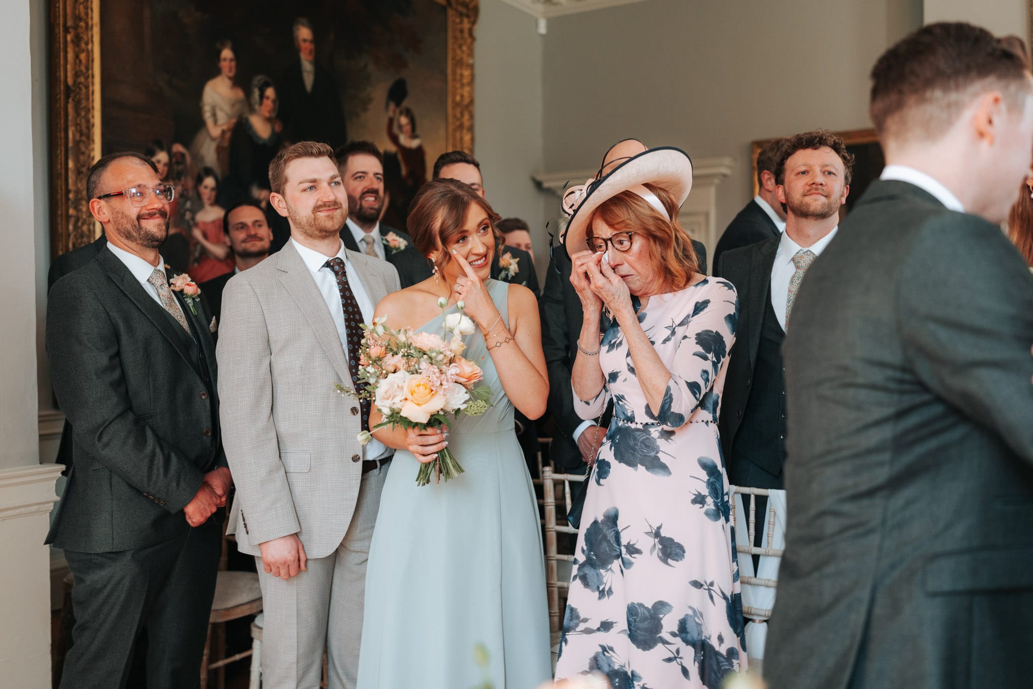 mother of bride in a floral dress wipes away a tear whilst the bridesmaid does that same inside Norwood Park's wedding ceremony room
