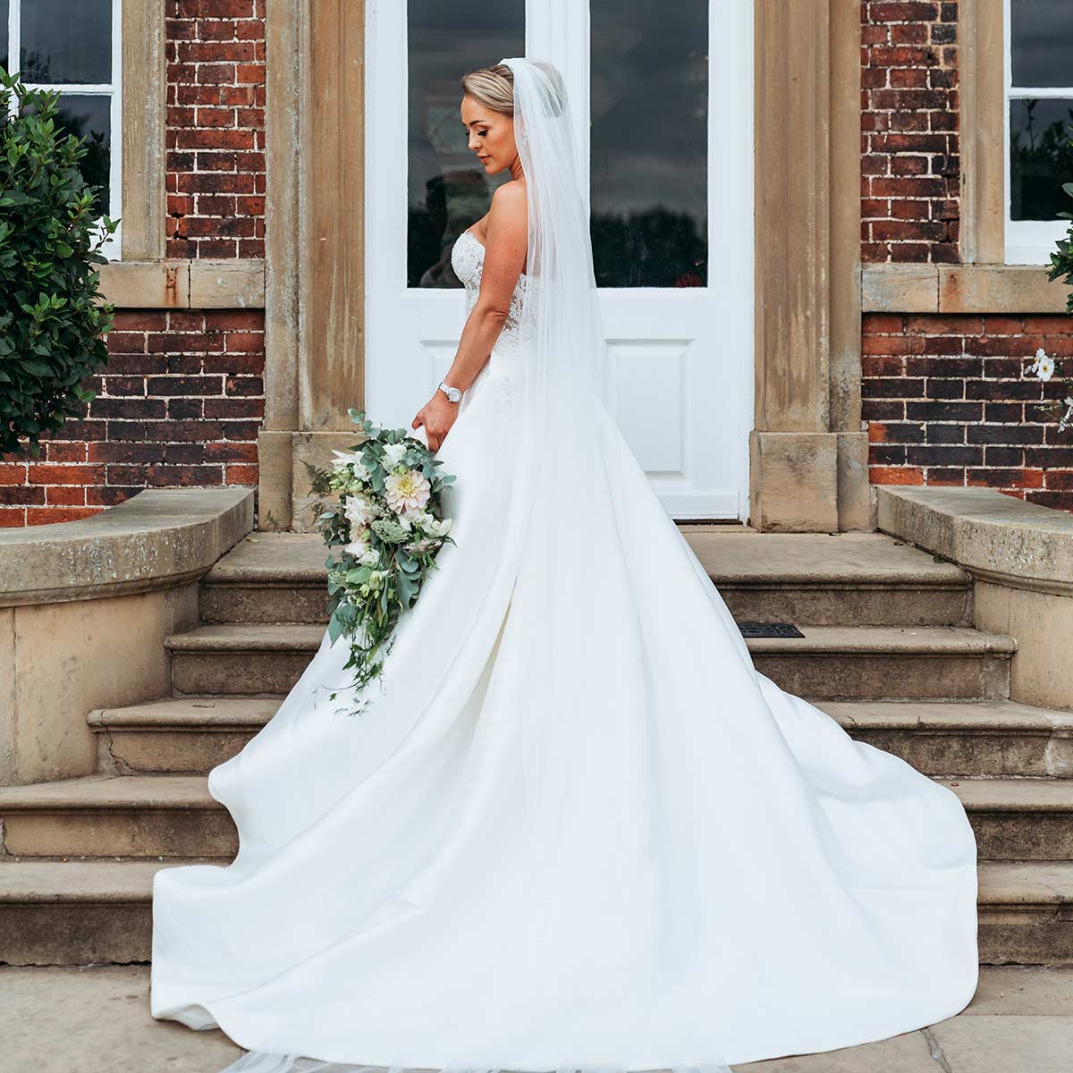 Beautiful bride standing on the steps of Norwood Park holding her bouquet